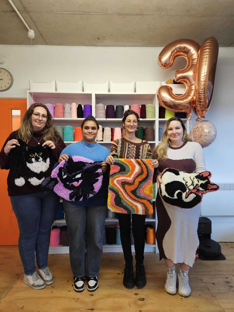 Four cheerful women celebrating a 30th birthday in a cozy studio, smiling as they show off their colourful, completed hand-tufted rugs.