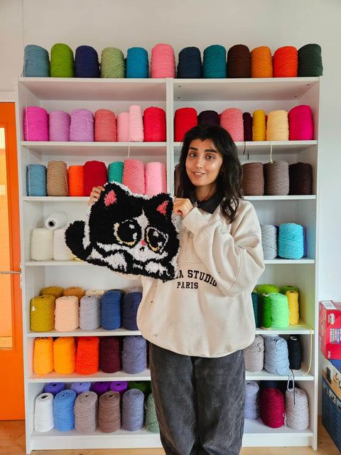 A women, proudly displaying their freshly tufted handmade cat rug in a vibrant studio setting.