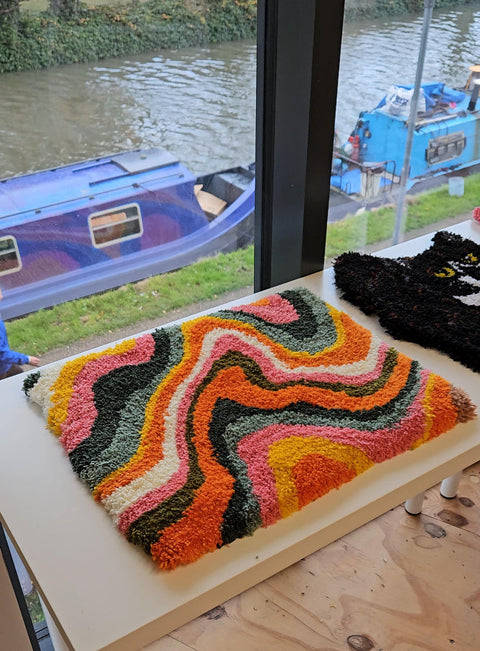 Colorful textured rug on a table with boats visible through a window in the background.