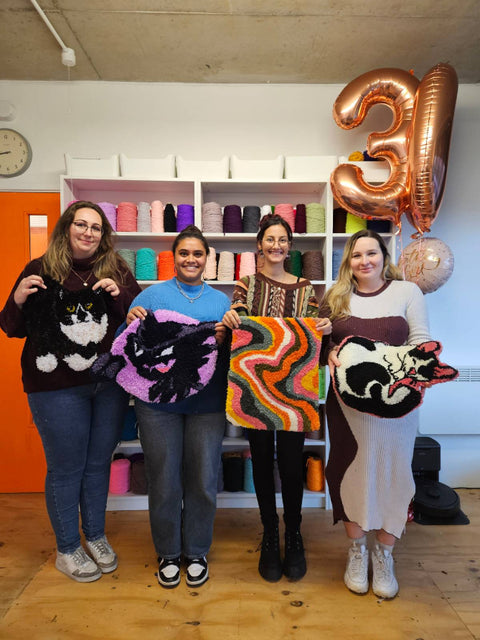 Four women holding Tufted rugs in a room with colorful yarn, celebrating a 30th birthday