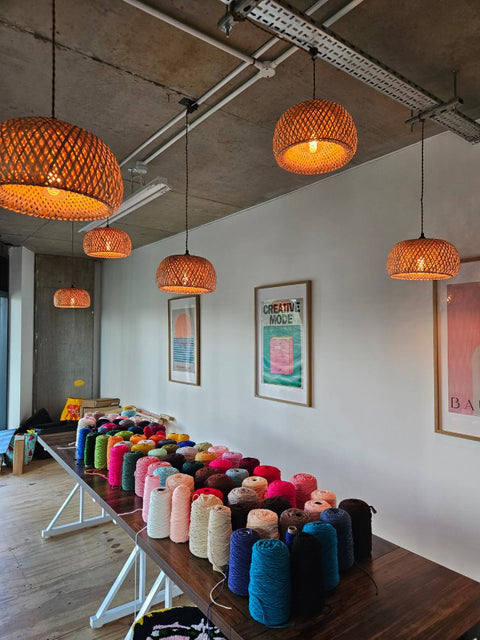 Colorful yarn spools on a table with woven pendant lights in a room.