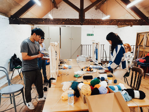 4 people working on a tufting rugs project in a workshop with wooden tables and tools.