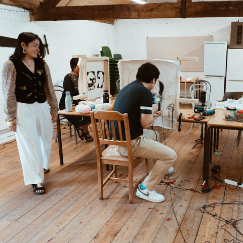 People working on tufted rugs in a creative studio while the instructor provides guidance.