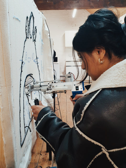 Person using a tufting gun to create a design on fabric.